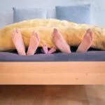 family of three lying on bed showing feet while covered with 1021051 1