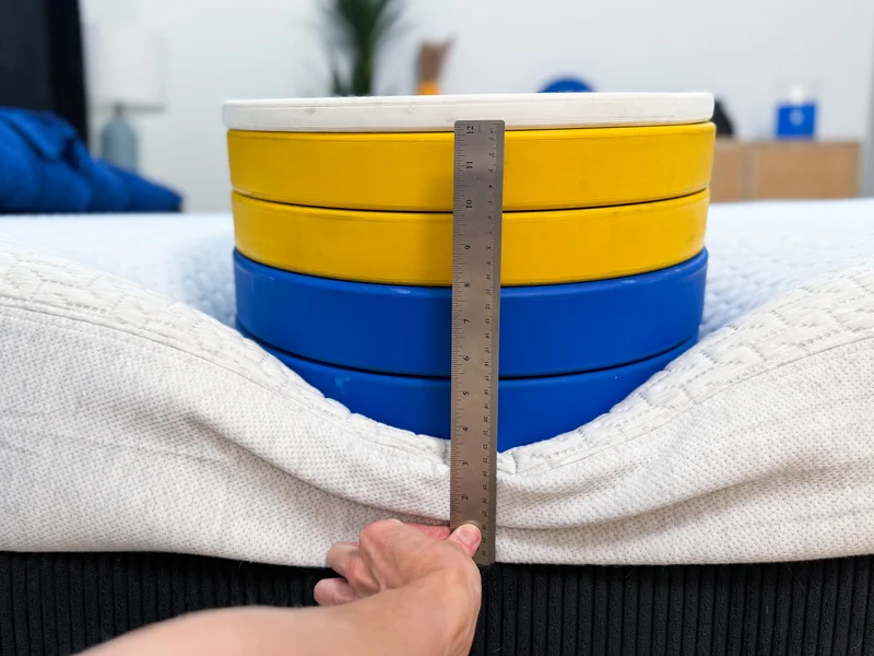 5 stacked weight plates on the edge of the Tuft and Needle Original mattress