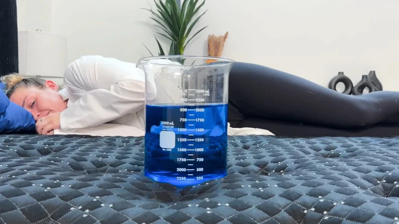 Product expert testing the motion isolation of the Beautyrest Black using container of blue liquid.